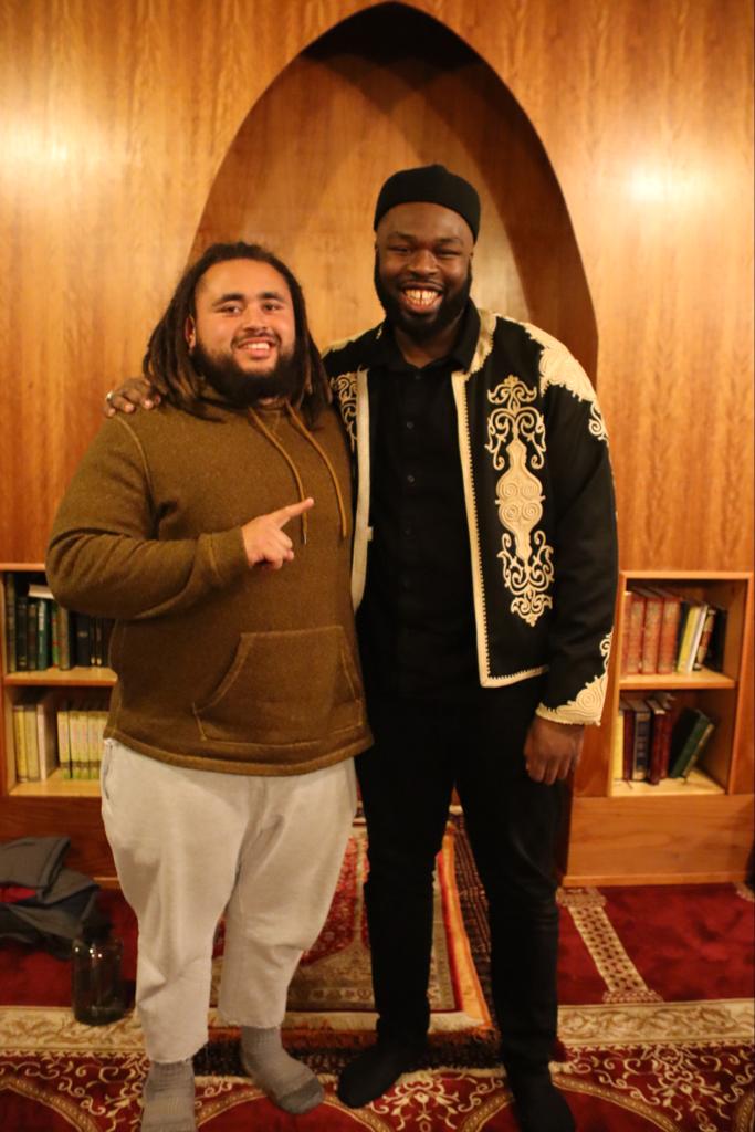 Two men standing next to each other in front of a bookshelf.